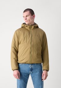 Khaki-Puffermantel mit Kapuze, Reißverschluss vorne, elastischen Bündchen und einer weichen Textur. Ergänzt durch ein Logodetail auf der Brust.