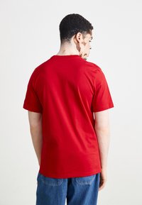 Piros pamut póló rövid ujjakkal és környakú fazonnal, hátulról mutatva. Simább textúrájú, egyszerű design, minták vagy kiegészítők nélkül.
