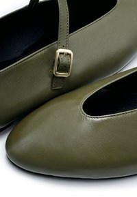 Olivgrüne Lederballerinas mit einer abgerundeten Spitze, die ein Ausschnittdesign und einen kleinen Riemen mit einer goldenen Schnalle zur Anpassung aufweisen.