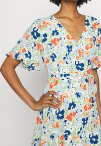 Květinové šaty s výstřihem do V, krátkými volánkovými rukávy, v světle modré barvě s oranžovými, zelenými a námořnickými květinovými vzory; zavazování v pase.