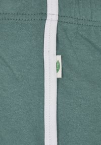 Close-up of green fabric with white trim and small tag showing a green leaf icon stitched into the seam.