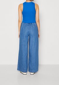 Blå beskuren tanktop i kombination med lösa, ljusblå denimbyxor med vida ben. Tyget är mjukt, med en avslappnad passform och elastisk midja.