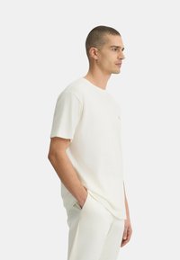 T-shirt a maniche corte color crema realizzato in tessuto morbido, con scollatura rotonda e un logo discreto sul petto. Vestibilità casual con silhouette rilassata.