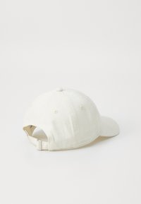 Casquette de baseball couleur crème avec une visière incurvée, en tissu doux, et sangle réglable à l'arrière. Comprend six œillets de ventilation et un bouton sur le haut.