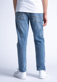 Jeans de mezclilla azul claro con un corte recto, dos bolsillos traseros y detalles de costura sutiles, combinados con zapatillas blancas.
