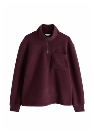 Pulover od flisa u boji šljive s dugim rukavima, visokim ovratnikom, polu-zip prednjim dijelom, rebrastim manžetama i jednim džepom na lijevoj strani prsiju.