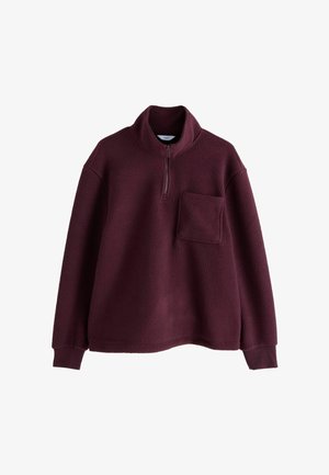 Plum-värinen fleece-pullover, jossa on pitkät hihat, korkea kaulus, puolivetoketju edessä, ribattu hihansuu ja yksi rintatasku vasemmalla puolella.