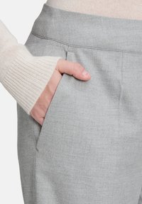 Szare eleganckie spodnie o gładkiej fakturze, z bocznymi kieszeniami. Ręka wsunięta jest do kieszeni, co podkreśla krój.