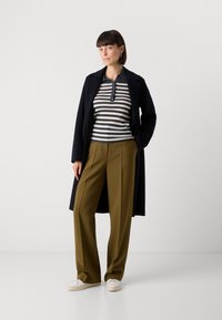 Manteau navy sur un polo à rayures noir et blanc, pantalon large olive, et baskets blanches. Textures lisses, design décontracté.