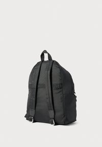 Melnas neilona mugursomas ar regulējamiem, polsterētiem siksnām un augšējo rokturi, rādīta no mugurpuses uz vienkārša gaiša fona.