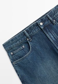 Jeans in denim blu scuro con passanti per cintura, chiusura con bottone in metallo, tasche anteriori e una piccola tasca portamonete su sfondo bianco.