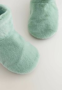 Pantofole morbide in peluche verde menta, con punta rotonda e risvolto alto. La texture è liscia e pelosa, offrendo calore e comfort.