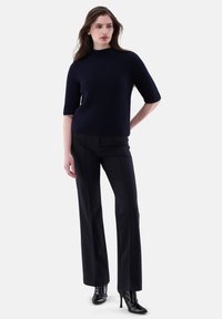 Navy-blaues ribbes Strickoberteil mit kurzen Ärmeln, kombiniert mit schwarzen, taillierten Hosen und spitzen schwarzen High Heels. Glatte Textur, moderne Silhouette.