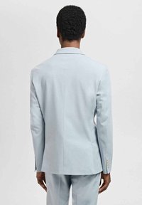 Jasnoniebieska marynarka o dopasowanym kroju, z wyraźnymi ramionami, pojedynczym rozcięciem oraz trzema guzikami na mankietach, wykonana z gładkiego materiału.