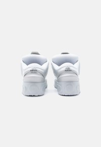 Adidași albi cu un finisaj neted, guler căptușit și accent gri în spate. Prezintă o vârf rotunjit și o talpă texturată.