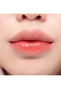 Gros plan sur des lèvres avec une teinte corail douce. Texture lisse avec une finition brillante et une forme bien définie. Pas de fissures ni de sécheresse visibles.