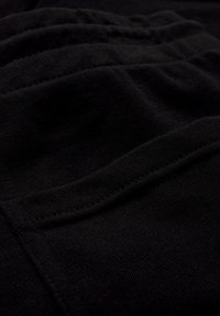 Gros plan sur un tissu noir texturé avec des coutures visibles et des plis subtils, probablement une partie d'un vêtement.