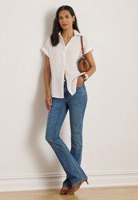 White linen short-sleeve shirt, blue flared jeans, brown leather handbag, and brown heeled shoes, posed against a neutral background.