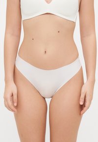 Weiße nahtlose Bikinihöschen aus glattem Material. Sie verfügen über einen tief sitzenden Schnitt und einen weichen Bund mit dezentem Branding an der Seite.