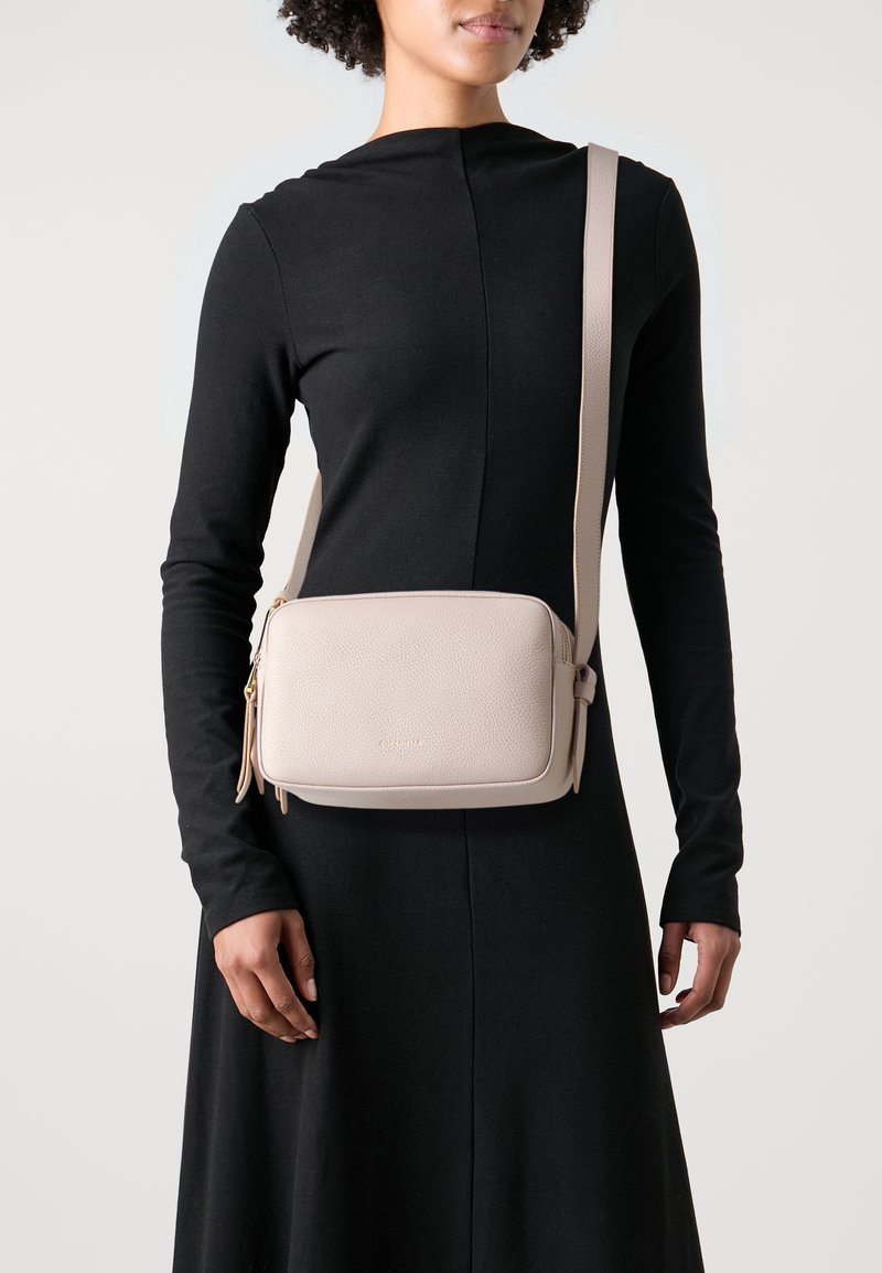 Crossbody bag in soft beige pebbled leather with a rectangular shape, zippered compartments, and a adjustable strap. Subtle brand logo displayed.