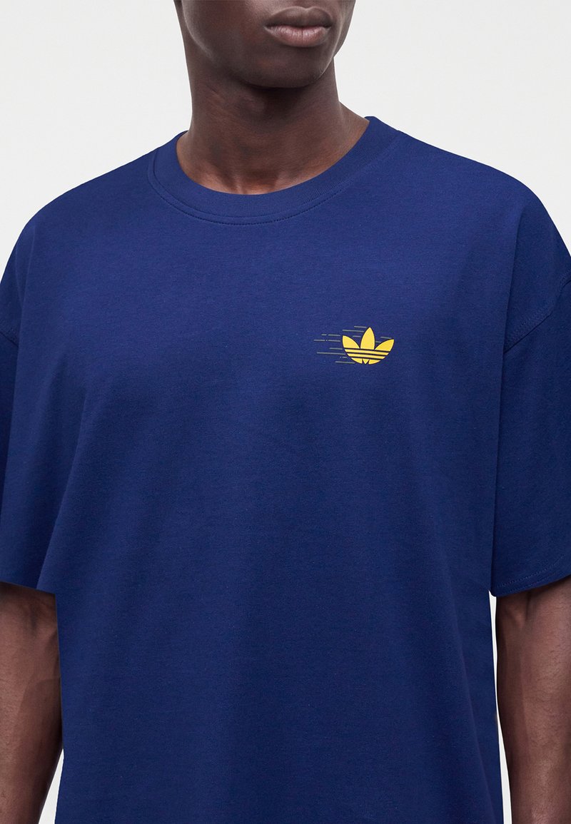 Hombre con camiseta azul con un pequeño logo estilizado de hoja amarilla en el pecho izquierdo.