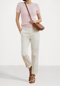 Růžový krátký svetr s kabelovým vzorem, kombinovaný s krémovými kalhotami s rovnými nohavicemi a hnědými sandály se štětkami; doplněn hnědou kabelkou přes rameno.