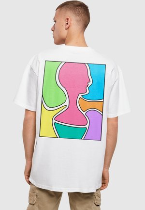 Hvid t-shirt med et farverigt abstrakt design på bagsiden med former, der ligner menneskeprofiler i teal, pink, gul, grøn og lilla.