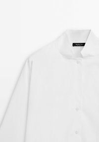Camicia bianca con colletto alla mandarina, realizzata in morbido cotone e con un design minimalista. Piccole bottoni lungo la parte anteriore.