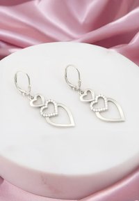 Silver hjärtformade örhängen med en lagerdesign och en glittrande rhinestone-accent. Strukturerad yta och lås av typ leverback.
