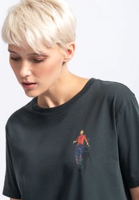 Donkergroene katoenen t-shirt met een kleurrijke print van een figuur op de voorkant. Korte mouwen en een ronde halslijn. Gladde textuur.