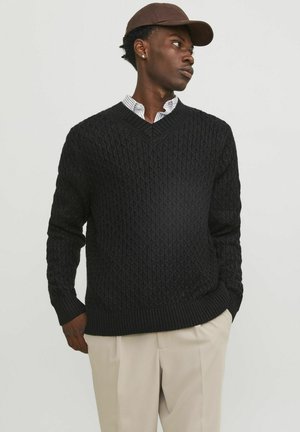 Black knitted sweater with a textured diamond pattern, v-neck design, and ribbed cuffs and hem. Paired with a collared shirt underneath.