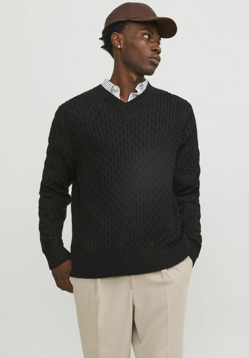Black knitted sweater with a textured diamond pattern, v-neck design, and ribbed cuffs and hem. Paired with a collared shirt underneath.