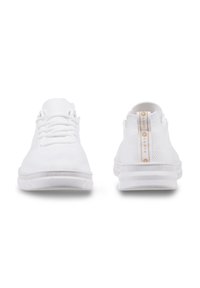 White athletic sneakers with a textured knit upper, round laces, and a looped heel tab featuring a logo printed in gold. Minimalist design.
