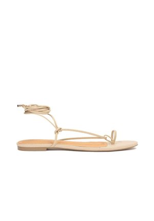 Beige flad sandal med tynd stroppedesign, der bindes omkring anklen, glat læderoverdel, minimalistisk form og gummisål.