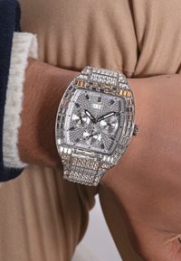 Sudraba pulkstenis ar taisnstūrveida ciparnīcu, kristāla rotājumiem, trim apakšciparnīcām un izsmalcinātu metāla aproci.