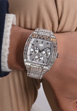 Silberne Uhr mit rechteckigem Zifferblatt, Kristallverzierung, drei Hilfszifferblättern und einem detaillierten Metallarmband.