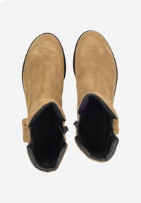 Para brązowych zamszowych botków za kostkę z czarną podszewką i bocznymi klamrami, widocznych z góry na jednolitym tle.