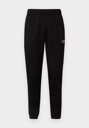 Pantalones de chándal negros con cintura elástica, puños ajustados y un pequeño logo amarillo en la parte superior de la pierna izquierda. Textura de tela suave y lisa.