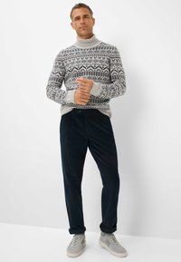 Maglione lavorato a maglia con un design a fantasia in grigio e blu navy, abbinato a pantaloni in velluto a coste blu scuro. Sneakers grigie con accenti chiari completano il look.