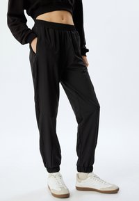 Zwarte, lichte joggerbroek met een elastische tailleband, zijzakken en geribde manchetten; gladde textuur en een relaxte pasvorm.
