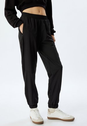 Zwarte, lichte joggerbroek met een elastische tailleband, zijzakken en geribde manchetten; gladde textuur en een relaxte pasvorm.
