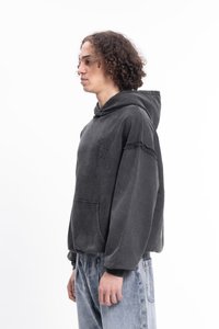 Felpa grigia scura con tasca anteriore, cappuccio e dettagli sfilacciati sulle maniche. Il tessuto sembra morbido con una vestibilità complessiva rilassata.