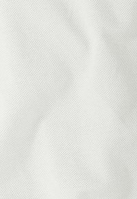 Tissu blanc texturé avec un motif fin tricoté, créant une surface lisse et douce, adapté aux vêtements ou à la tapisserie.