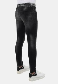 Zwarte denim skinny jeans met vervaagde accenten, vijf-pocketdesign en een leren merkpatch op de tailleband. Draagt met witte sneakers.