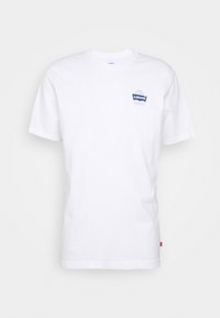 Bílá bavlněná tričko s kulatým výstřihem a krátkými rukávy, se modrou nášivkou loga Levi's na levé části hrudi.