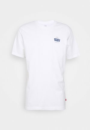 T-shirt en coton blanc avec un col rond et des manches courtes, présentant une patch de logo bleu Levi's sur la zone de la poitrine gauche.