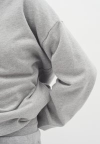 Grå sweatshirt med avslappnad passform, ribbad nederkant och oversized ärmar, tillverkad av mjukt tyg med en slät textur.