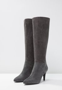 Bottes à talons hauts en suède gris avec un upper ajusté, bout pointu et finition texturée. La conception présente une silhouette élégante et moderne.