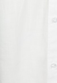 Nabij een witte linnen blouse, met een fijne textuur, subtiele weefstructuur en een knopenlijst met transparante knopen.