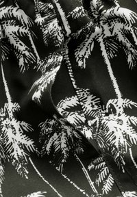 Tissu noir orné d'un imprimé de palmier blanc avec des feuilles détaillées. Texture lisse avec des coutures et des plis visibles.